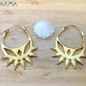 May include: A pair of gold-toned brass earrings with a geometric design. The earrings are shaped like a sun with a starburst pattern.