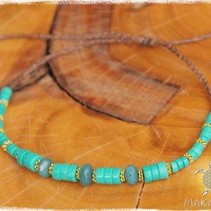 May include: A turquoise and gold beaded necklace with a brown cord. The necklace has a turquoise and gold bead pattern with larger turquoise beads in the center.