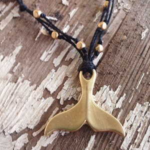 May include: A gold whale tail pendant necklace with black cord and gold beads.