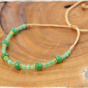 May include: A green gemstone necklace with gold accents on a brown wooden surface. The necklace is made with a simple string and has a sliding knot closure.