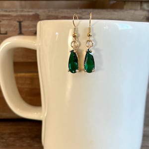 May include: A pair of gold dangle earrings with teardrop-shaped green gemstones.