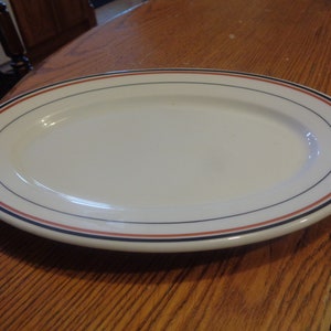 May include: A white oval platter with a blue and orange trim. The platter is on a wooden surface.