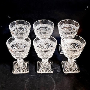 Puede incluir: Juego de seis copas de postre de cristal transparente. Cada copa tiene una base cuadrada con diseño de rayos de sol, un tallo texturizado y un cuenco redondo con un patrón de diamantes. Dispuestas sobre una superficie negra.