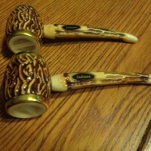 May include: Two ceramic salt and pepper shakers shaped like pipes. The shakers are brown and white with a gold trim. The shakers have the word "Indiana" on them.