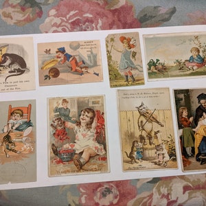 May include: A collection of nine vintage trade cards featuring illustrations of children and cats. The cards depict scenes such as a cat pulling a chestnut out of a fire, a child playing with a cat, and a cat playing the violin. The cards are printed on thick paper with vibrant colors and intricate details.