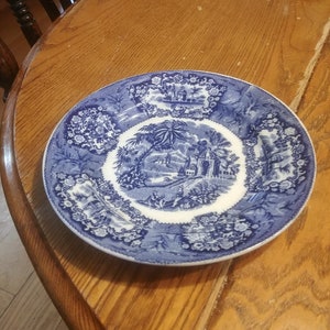 Könnte beinhalten: Ein blauer und weißer Porzellanteller mit einem Blumendesign und einer zentralen Szene mit einem Gebäude und Palmen.