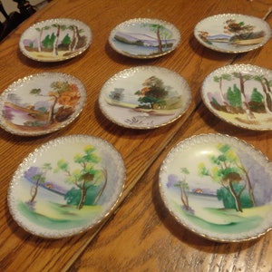 Eight Ucagco 4" Hand Painted Hanging Plates. Seven Different Scenes, Loop Edging with Gold. No Wear Evident. 7 have Foil Label. INV#0807