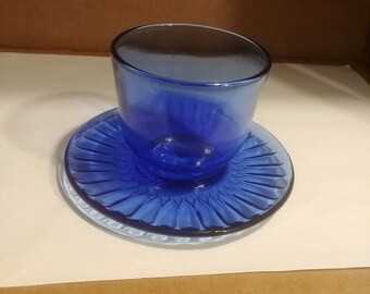 May include: A cobalt blue glass cup and saucer set. The saucer has a fluted design.