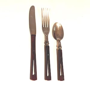 May include: A three-piece flatware set consisting of a knife, a fork, and a spoon. Each utensil features a metallic silver-toned head and a dark brown handle with a distinct elongated cutout near the base of the handle, providing a uniform look.