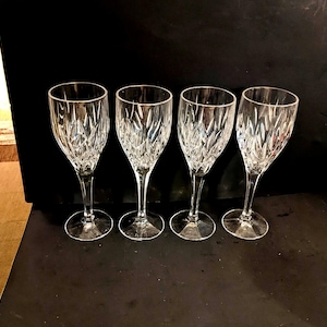 Può includere: Quattro calici da vino in cristallo trasparente con un motivo strutturato e dettagliato. I calici hanno un design classico con un gambo sottile e una base rotonda. Lo sfondo è nero pieno, evidenziando la chiarezza e il design intricato del vetro.