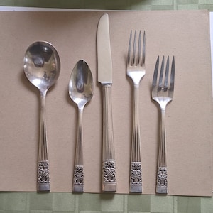 Puede incluir: Un juego de cinco cubiertos de plata plateada, que incluye un cuchillo, dos tenedores y dos cucharas. Los mangos están decorados con un diseño floral.