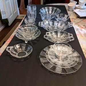 May include: A collection of clear glass serving dishes and glassware, including bowls, cups, and plates. The glassware features a ribbed design. Some pieces have handles. The items are arranged on a black surface.