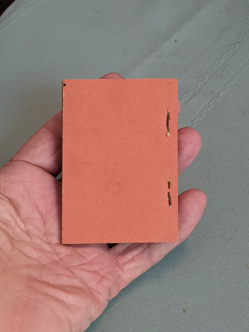 Pode incluir: Um pequeno livro retangular de cor laranja com encaderna&ccedil;&atilde;o costurada.