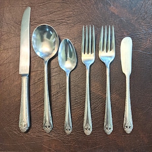 Könnte beinhalten: Ein Set aus sechs versilberten Besteckteilen, bestehend aus einem Buttermesser, einem Essmesser, zwei Gabeln und zwei Löffeln. Das Besteck hat ein verziertes Design mit einem floralen Muster.