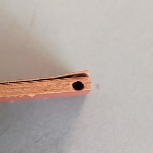 Pode incluir: Close-up da lombada de um livro com um furo perfurado. O livro &eacute; encadernado em papel castanho avermelhado.