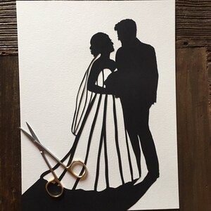 May include: A black paper silhouette of a bride and groom standing close together. The bride is wearing a long dress with a veil. The groom is wearing a suit. The silhouette is cut out of white paper.