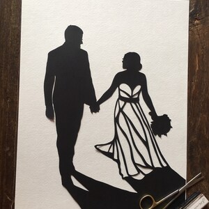 May include: Black paper cut-out silhouette of a bride and groom holding hands. The bride is wearing a gown with a detailed design. The groom is wearing a suit. The artwork is on a white background.