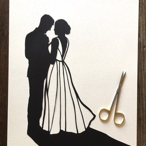 May include: A black paper silhouette of a couple dancing, the woman in a flowing gown, the man in a suit. The silhouette is on a white background with a pair of gold scissors in the lower right corner.