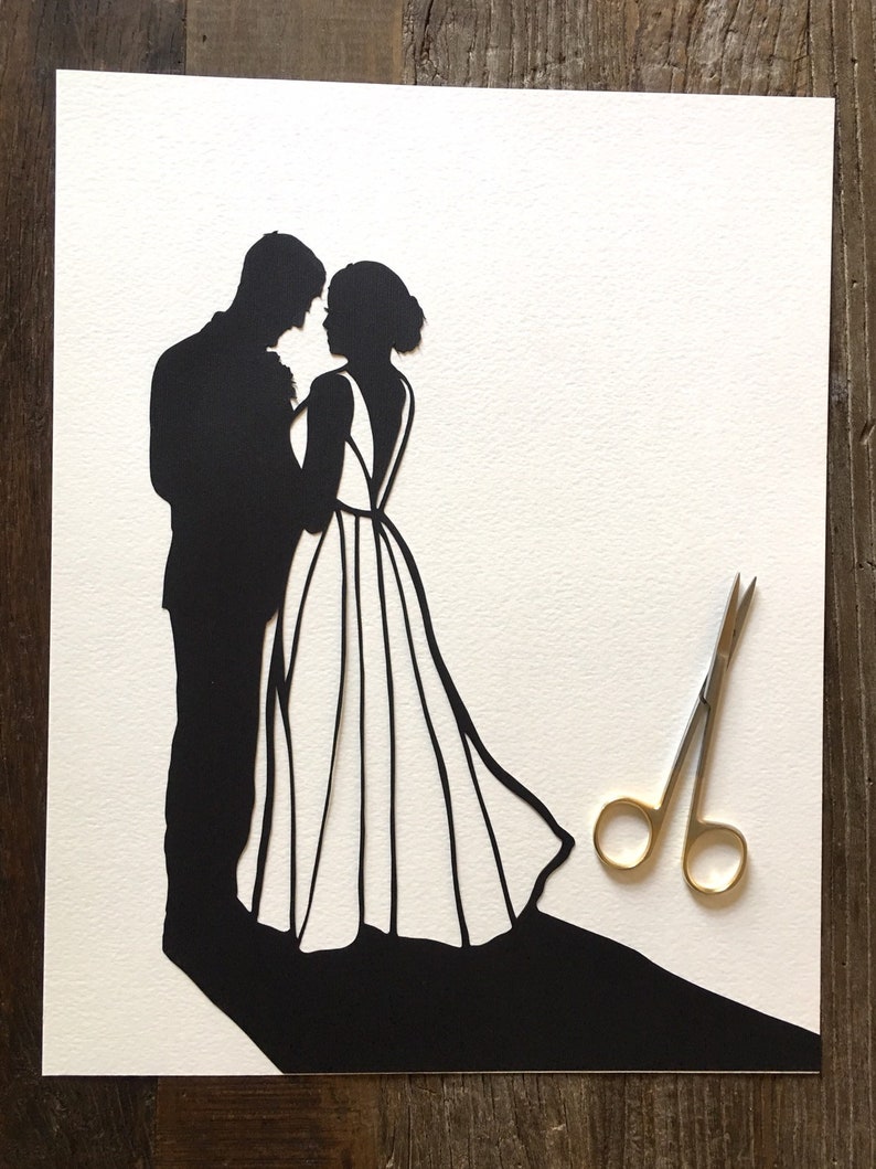 May include: A black paper silhouette of a couple dancing, the woman in a flowing gown, the man in a suit. The silhouette is on a white background with a pair of gold scissors in the lower right corner.