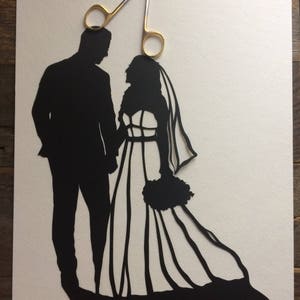May include: A black paper silhouette of a bride and groom holding hands, with a pair of gold scissors above them.