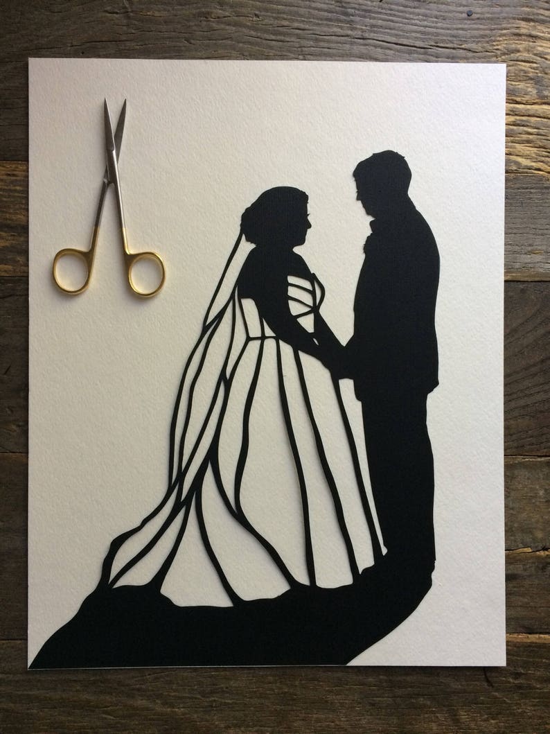May include: A black paper silhouette of a bride and groom standing side by side. The bride is wearing a long gown with a veil and the groom is wearing a suit. The silhouette is cut out of white paper and is set against a white background.