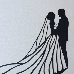 May include: Black silhouette paper cut-out of a bride and groom. The bride is wearing a long gown with a veil and the groom is wearing a suit. The couple is facing each other and holding hands.