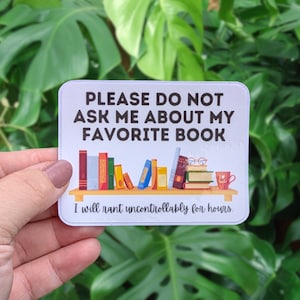 May include: White sign with black text that reads "PLEASE DO NOT ASK ME ABOUT MY FAVORITE BOOK I will rant uncontrollably for hours."  The sign features a bookshelf with a stack of books, a pair of glasses, and a mug that says "I love books".