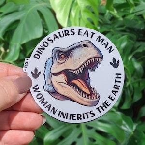 May include: A white round sticker with a black dinosaur illustration and the text "Dinosaurs Eat Man Woman Inherits The Earth".