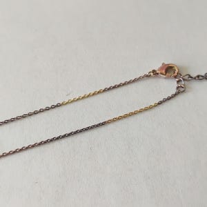May include: A delicate two-tone chain necklace featuring alternating segments of dark gunmetal grey and bright gold-colored metal links. The necklace includes a small lobster claw clasp and a short extender chain at the end for adjustable length.