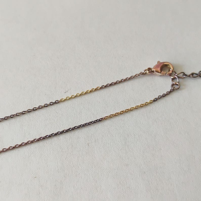 May include: A delicate two-tone chain necklace featuring alternating segments of dark gunmetal grey and bright gold-colored metal links. The necklace includes a small lobster claw clasp and a short extender chain at the end for adjustable length.