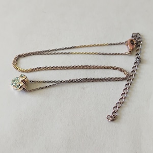 May include: A delicate necklace featuring a metallic chain with a rose gold tone and a small pendant shaped like a paw print. The pendant is encrusted with tiny, light blue crystals. The necklace includes a lobster claw clasp and an extender chain.