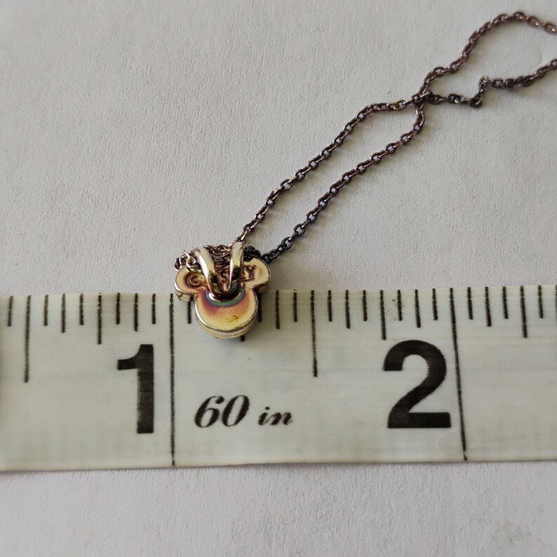 May include: A metallic pendant shaped like a stylized mouse head attached to a thin chain, positioned against a white measuring tape that shows the pendant width is approximately 0.5 inches. The pendant has a smooth, reflective surface.