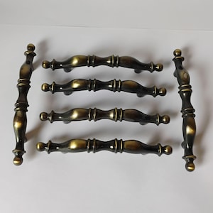 May include: A set of six cabinet pulls featuring a dark bronze finish with highlighted gold-toned edges. The hardware consists of four horizontal handles and two vertical handles, each with a curved, multi-segmented design and rounded ends.