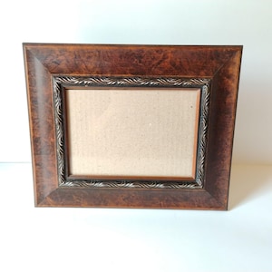 May include: A rectangular picture frame featuring a dark brown, mottled faux-wood finish on the wide outer border. The inner edge is decorated with a raised, repeating wave-like pattern in a dark metallic tone, surrounding a plain cardboard insert.
