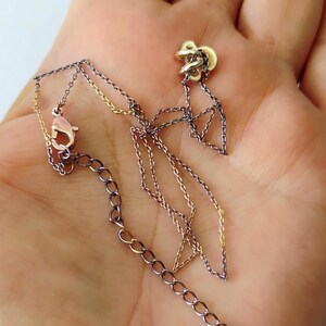 May include: A delicate necklace featuring a mix of dark gunmetal and bright gold-tone chain links. The piece includes a small, textured gold-tone charm at one end and a lobster claw clasp with an adjustable extender chain for a secure fit.