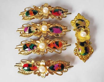 May include: A set of five gold-toned hair clips featuring intricate metalwork, central white faux pearls, and teardrop-shaped accents with multicolored patterns in shades of green, orange, purple, and black, arranged in a horizontal and vertical layout.