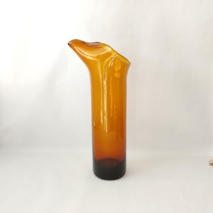 May include: A tall, amber-colored glass vase with a unique, curved top. The vase has a dark brown base and a smooth, glossy finish. The design is modern and elegant, suitable for displaying flowers or as a decorative piece.