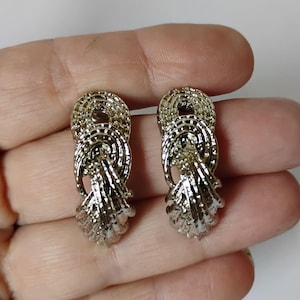 May include: A pair of silver-toned metal earrings featuring a textured, layered design. Each earring consists of a circular top section connected to a cascading, fan-like bottom piece with intricate, grooved detailing throughout the surface.