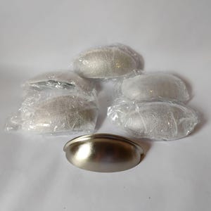 May include: A set of five semi-circular cup drawer pulls with a brushed nickel finish. One pull is unwrapped and positioned in the foreground, while four additional pulls remain individually sealed in clear plastic protective packaging.