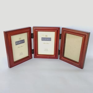 May include: A hinged, wooden photo frame with three panels. The frame is a rich, reddish-brown color. Each panel is designed to hold a 3x5 inch photograph. The brand name "BURNES" is printed on a blue and white label in the center panel.