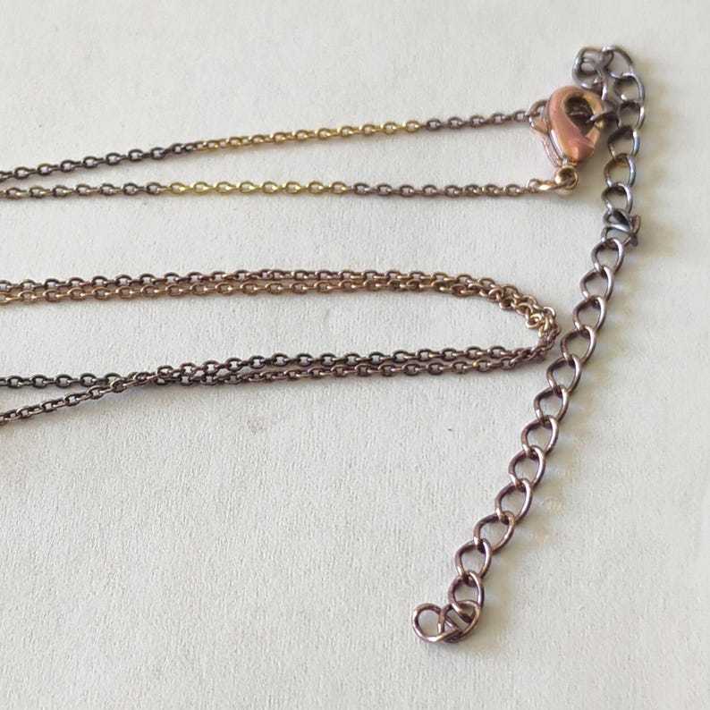 May include: A multi-strand necklace chain featuring a mix of gold-toned and dark metallic links. The design includes a lobster claw clasp and an adjustable extender chain with larger oval links, providing a versatile length for the jewelry piece.