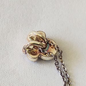 May include: A gold-toned metal pendant shaped like a three-petaled flower or clover, featuring a central circular detail and a polished finish. The pendant is attached to a delicate, thin metal chain link necklace that extends downward from the piece.