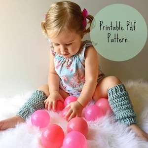Puede incluir: Una niña con un body floral y calentadores de piernas de ganchillo rodeada de bolas rosas. El texto "Printable Pdf Pattern" es visible en un círculo verde. Los calentadores son de color verde claro.