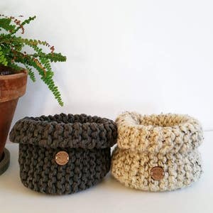 Pu&ograve; includere: Due cesti all'uncinetto, uno in grigio scuro e uno in beige, con un bottone in legno su ciascuno.