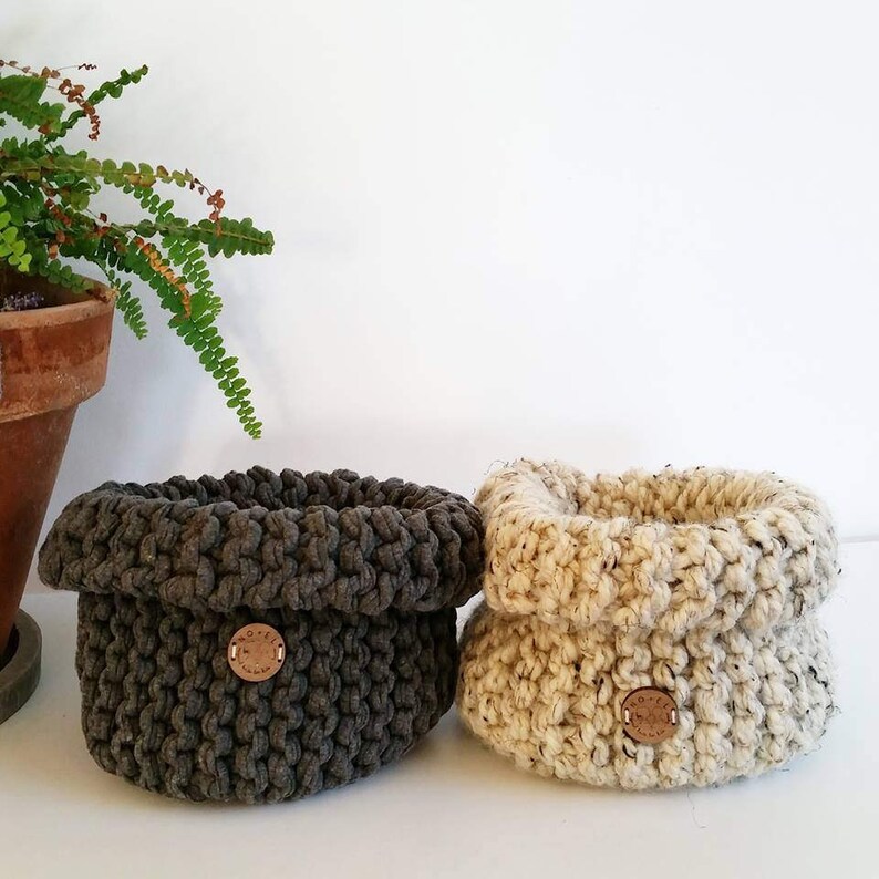 Pu&ograve; includere: Due cesti all'uncinetto, uno in grigio scuro e uno in beige, con un bottone in legno su ciascuno.