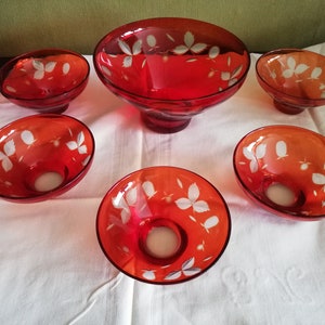 Könnte beinhalten: Satz von sechs roten Glasschalen mit weißen, geätzten Blattmotiven. Die Schalen sind in verschiedenen Größen und auf einer weißen Tischdecke angeordnet.