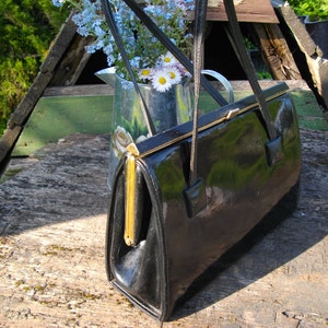 Peut inclure: Une pochette en cuir noir avec une fermeture dorée et une longue bandoulière. La pochette est posée sur une surface en bois.