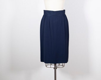 May include: A navy blue pencil skirt displayed on a mannequin. The skirt has a high waist with a unique folded design and a straight, knee-length hemline. The skirt is made of a smooth, solid fabric and is suitable for professional or formal wear.