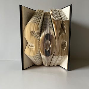 May include: A book art sculpture of the word "sole" created by folding the pages of a book. The sculpture is made from a book with a black cover.