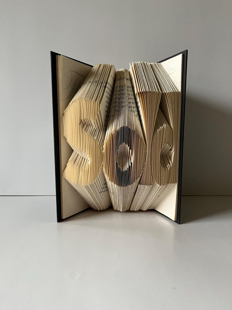 May include: A book art sculpture of the word "sole" created by folding the pages of a book. The sculpture is made from a book with a black cover.